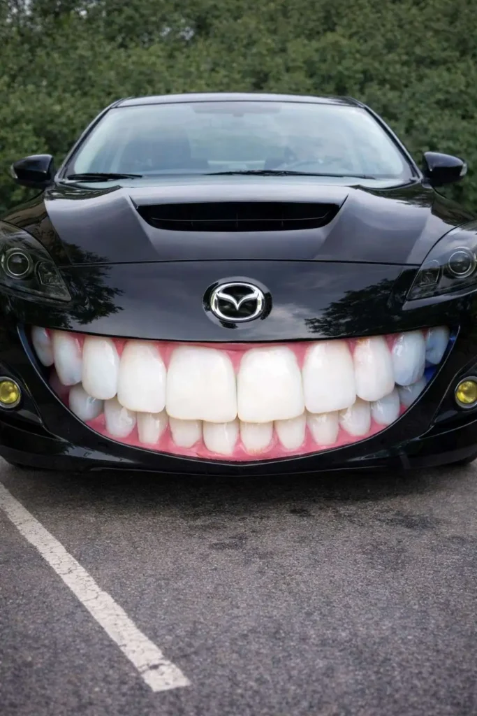 Black Mazda sports car modified with a giant smiling mouth and realistic human teeth on the front bumper