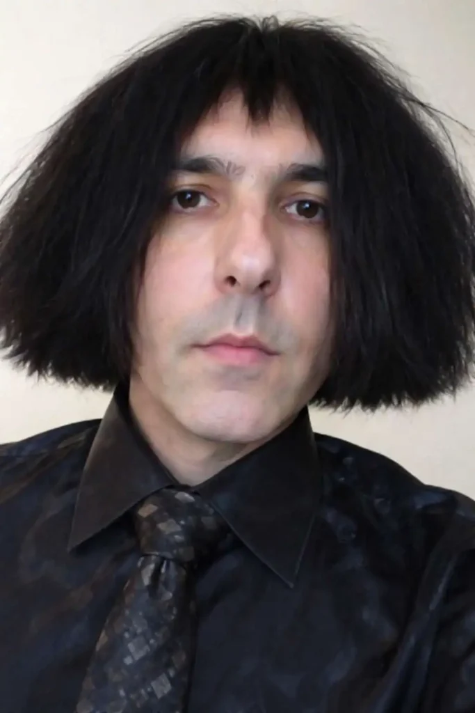 Person wearing a blunt black bob haircut with uneven ends and bangs, styled to resemble a dramatic and unconventional hairstyle look