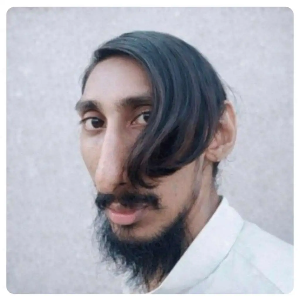 Person with a side-swept hairstyle covering one eye, styled with a thin mustache and pointed beard for an artistic and unconventional appearance